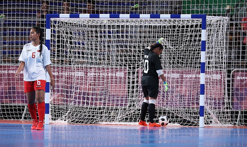 female soccer player and goalkeepr in front of a futsal goal